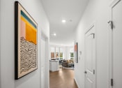 Thumbnail 9 of 30 - A hallway with a large painting on the wall and a view of a living room through the door.