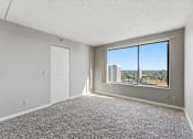 Thumbnail 109 of 151 - A room with a carpeted floor, a door, and a window overlooking a cityscape.