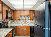 Thumbnail 107 of 151 - A kitchen with a black refrigerator and wooden cabinets.