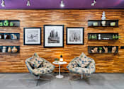 Thumbnail 83 of 151 - Two chairs and a table are in front of a wooden wall with pictures and shelves.
