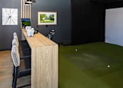 Thumbnail 43 of 46 - A room with a wooden desk and a golf ball on the green carpet.