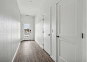 Thumbnail 24 of 26 - A long hallway with white doors and wood floors.