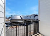 Thumbnail 9 of 27 - A view from a balcony looking out at a parking lot and a building.
