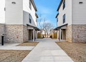 Thumbnail 16 of 27 - A long concrete walkway separates two buildings with stone pillars.