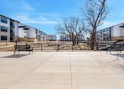 Thumbnail 15 of 27 - A concrete courtyard with benches and a fence in front of apartment buildings.