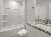 Thumbnail 12 of 19 - A white bathroom with a marble counter top and a white toilet.