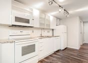 Thumbnail 13 of 32 - A kitchen with white appliances and wooden floors.