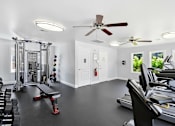 Thumbnail 18 of 28 - A gym with treadmills, weights, and a bench press.