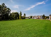 Thumbnail 26 of 29 - A large grassy field with trees and a building in the background.