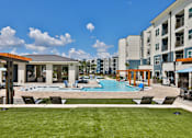 Thumbnail 20 of 32 - A swimming pool surrounded by lounge chairs and a building in the background.
