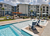 Thumbnail 18 of 32 - A swimming pool with a bench and umbrella in front of apartment buildings.