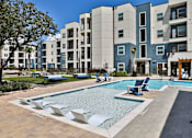 Thumbnail 16 of 32 - A swimming pool surrounded by lounge chairs and a building in the background.