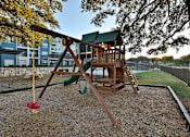 Thumbnail 27 of 32 - A wooden swing set with a red swing sits in a gravel backyard.