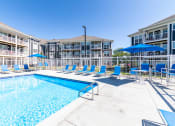Thumbnail 27 of 30 - a swimming pool with blue chairs and umbrellas in front of a building