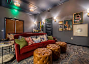 Thumbnail 26 of 43 - A living room with a red couch, a coffee table, and a green exit sign on the wall.