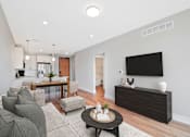Thumbnail 36 of 38 - A modern living room with a grey sofa, a wooden coffee table, and a flat-screen TV mounted on the wall.