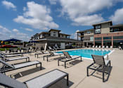 Thumbnail 35 of 50 - A pool area with sun loungers and a building in the background.