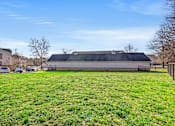 Thumbnail 38 of 42 - A large grassy field with a building in the background.