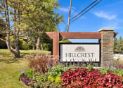 Thumbnail 32 of 38 - a sign for hillcrest apartments in front of a garden and trees