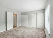 Thumbnail 37 of 45 - A room with white walls and a carpeted floor with four closets.