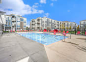 Thumbnail 6 of 27 - a swimming pool with red chairs and an apartment building in the background
