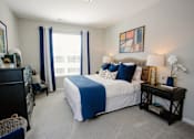 Thumbnail 10 of 43 - A bedroom with a bed, nightstand, and window with blue curtains.