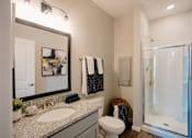 Thumbnail 15 of 43 - A bathroom with a toilet, sink, mirror, and a glass shower door.
