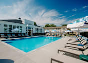 Thumbnail 35 of 43 - A large swimming pool area with sun loungers and a building in the background.