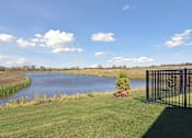Thumbnail 27 of 28 - A small pond in a grassy field with a black fence on the right side.