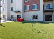 Thumbnail 9 of 17 - A playground with a red and blue swing set and a green lawn.