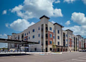 Thumbnail 10 of 17 - A large apartment complex with a parking lot in front.