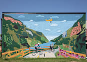 Thumbnail 17 of 17 - A mural depicts a cyclist and a pedestrian on a path through a mountainous landscape.