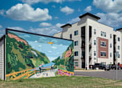 Thumbnail 16 of 17 - A mural of a person riding a bike is painted on the side of a building.