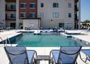 Thumbnail 4 of 17 - A pool surrounded by chairs and tables in front of a building.