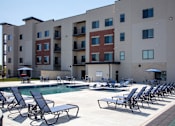 Thumbnail 5 of 17 - A pool area with chairs and a building in the background.