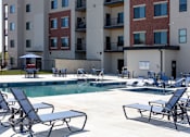 Thumbnail 6 of 17 - A pool area with chairs and a building in the background.
