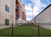 Thumbnail 14 of 17 - A black fence surrounds a green field in front of a building.