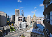 Thumbnail 41 of 41 - A cityscape with a mix of modern and older buildings, a clear blue sky, and a road with moving vehicles.