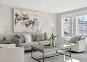 Thumbnail 15 of 44 - A living room with a grey couch, a coffee table, and a large painting on the wall.
