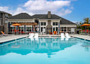 Thumbnail 25 of 26 - A swimming pool in front of a house with orange chairs around it.
