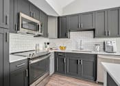 Thumbnail 5 of 42 - A kitchen with black cabinets and a white backsplash.