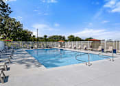 Thumbnail 23 of 53 - A large outdoor swimming pool surrounded by sun loungers and trees.