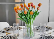 Thumbnail 7 of 44 - A table set with plates and glasses with a vase of orange tulips in the center.