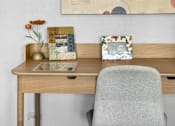 Thumbnail 14 of 44 - A painting hangs on a wall above a desk with a chair and some picture frames.