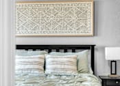 Thumbnail 17 of 44 - A bed with a black headboard and a white pillow with a geometric patterned artwork above it.