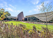 Thumbnail 31 of 44 - A modern building with a curved roof and a tall tree in the foreground.