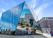 Thumbnail 32 of 44 - A modern building with a blue glass facade and a triangular shape.