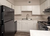 Thumbnail 1 of 15 - A black refrigerator stands in a kitchen with white cabinets and a sink.