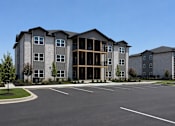 Thumbnail 3 of 4 - A large, modern apartment complex with a parking lot in front.