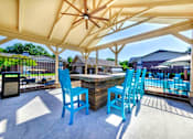 Thumbnail 20 of 24 - A patio with blue chairs and a table under a canopy.